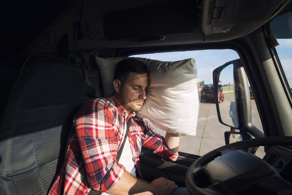 Водитель грузовика спит в кабине своего грузовика из-за дальних поездок и переутомления.